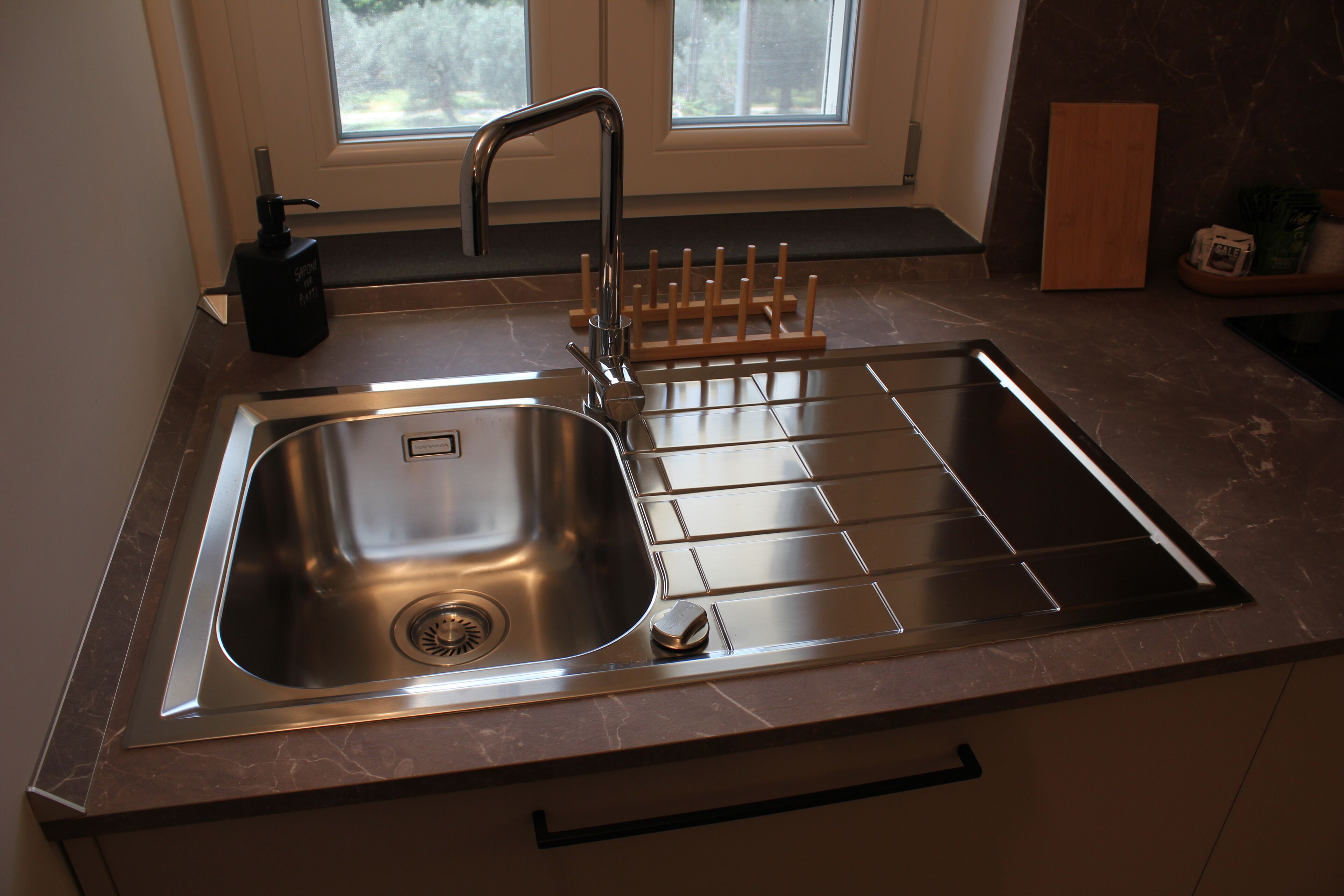 A kitchen with a stainless steel sink, a faucet, and a wooden rack for utensils.