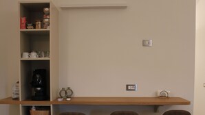 Eine Küchenzeile mit einer Kaffeemaschine, einem Regal mit Gegenständen und einer Holztresen mit drei Stühlen.