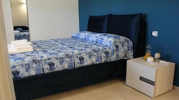 A bed with a patterned bedspread, a bedside table with a lamp, and a mirror on the wall.