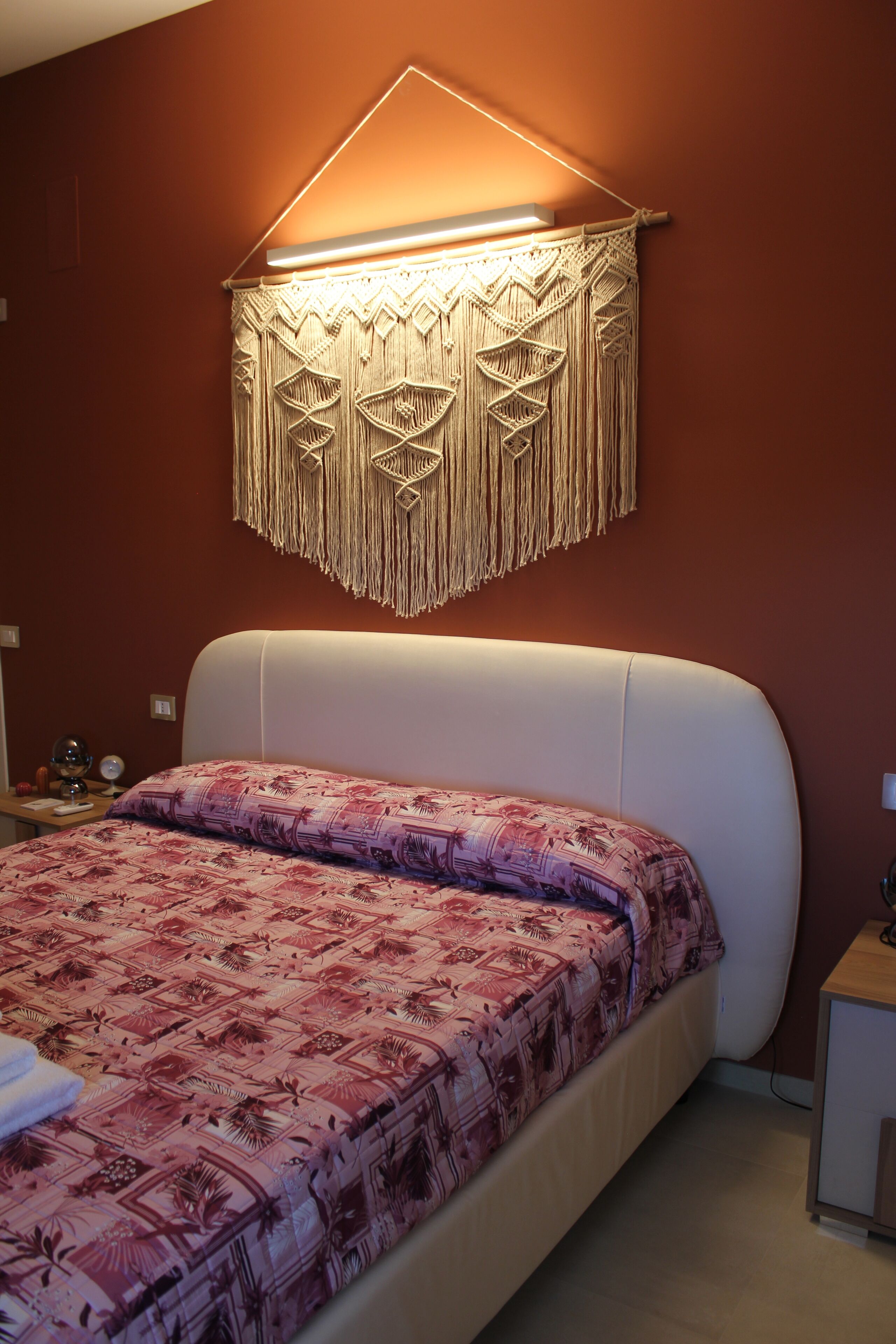 Une chambre à coucher avec un lit, une décoration murale en macramé et une table de chevet.