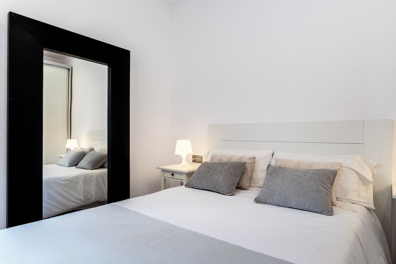 Een hotelkamer met een groot bed, een nachtkastje met een lamp en een spiegel.
