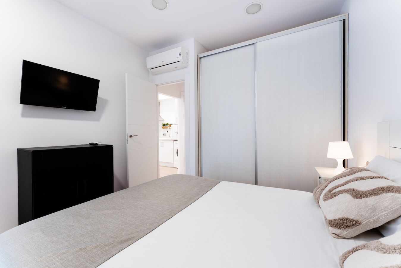 Un dormitorio con cama, televisor, armario y mesita de noche con lámpara.