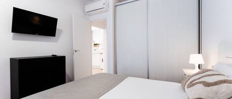Un dormitorio con cama, televisor, armario y mesita de noche con lámpara.