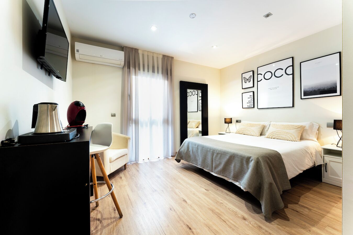 Habitación de hotel moderna con cama, mesita de noche, lámpara y escritorio con cafetera.
