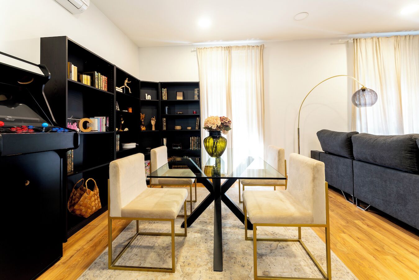 Un salon moderne avec une table à manger en verre, deux chaises, un canapé, une bibliothèque noire et un lampadaire.