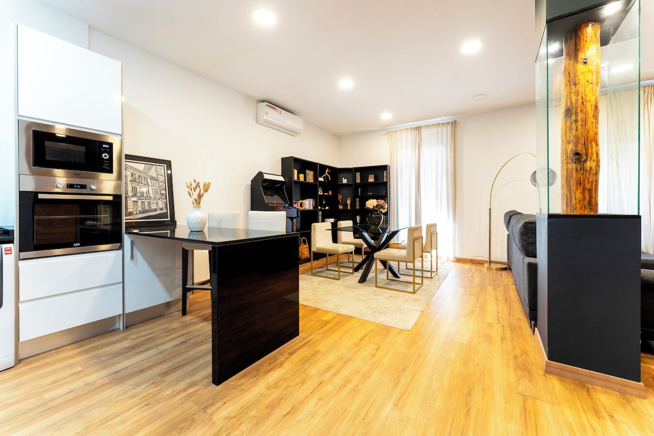 A modern kitchen with built-in appliances, a dining area with a glass table, and a black bookshelf.