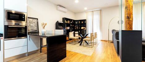 A modern kitchen with built-in appliances, a dining area with a glass table, and a black bookshelf.