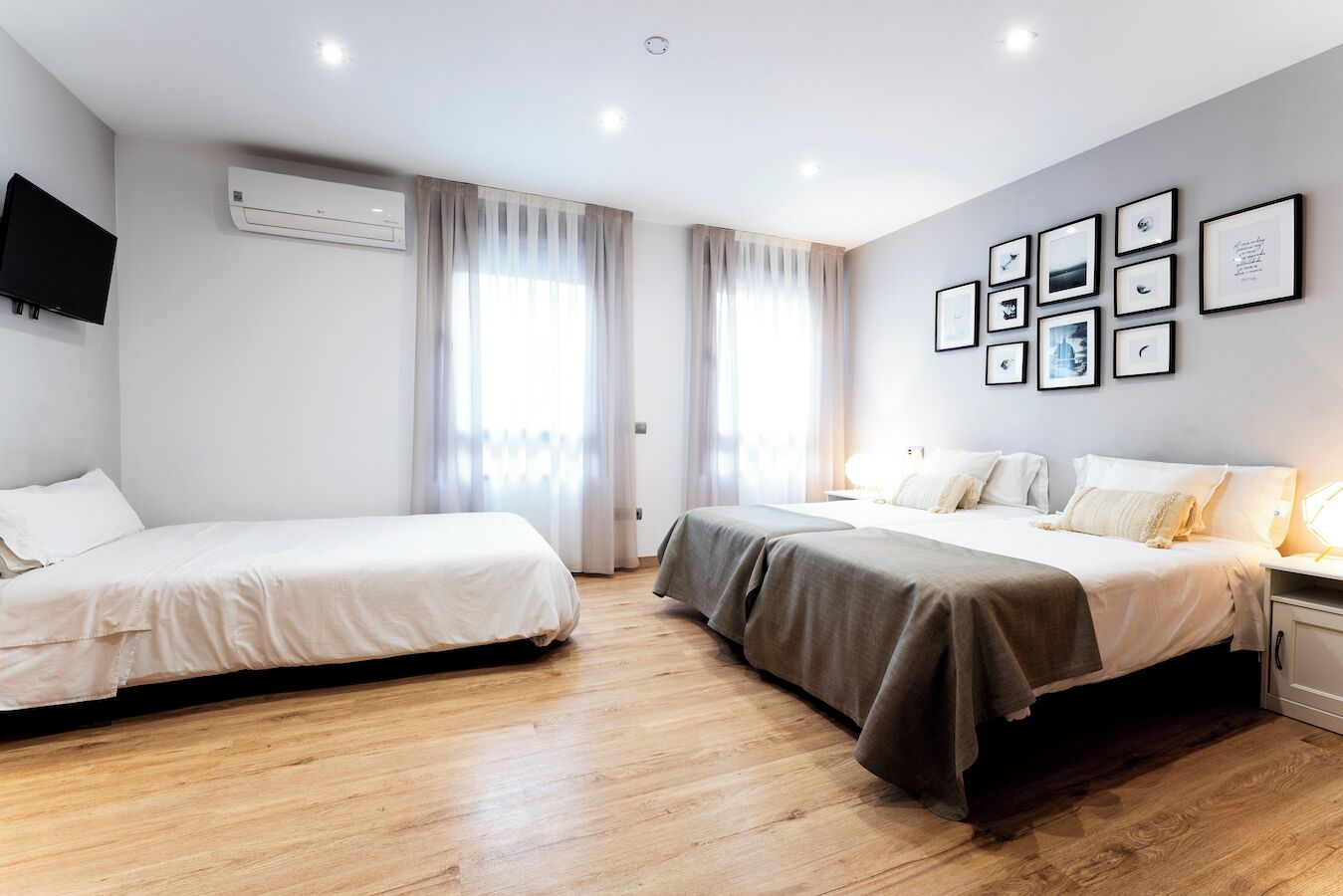 A hotel room with two beds, a flat-screen TV, an air conditioning unit, and framed pictures on the wall.