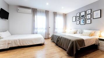 A hotel room with two beds, a flat-screen TV, an air conditioning unit, and framed pictures on the wall.