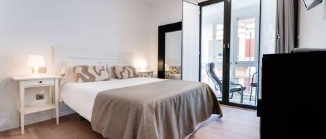 Un dormitorio con cama, mesitas de noche, televisor y un balcón con una silla.