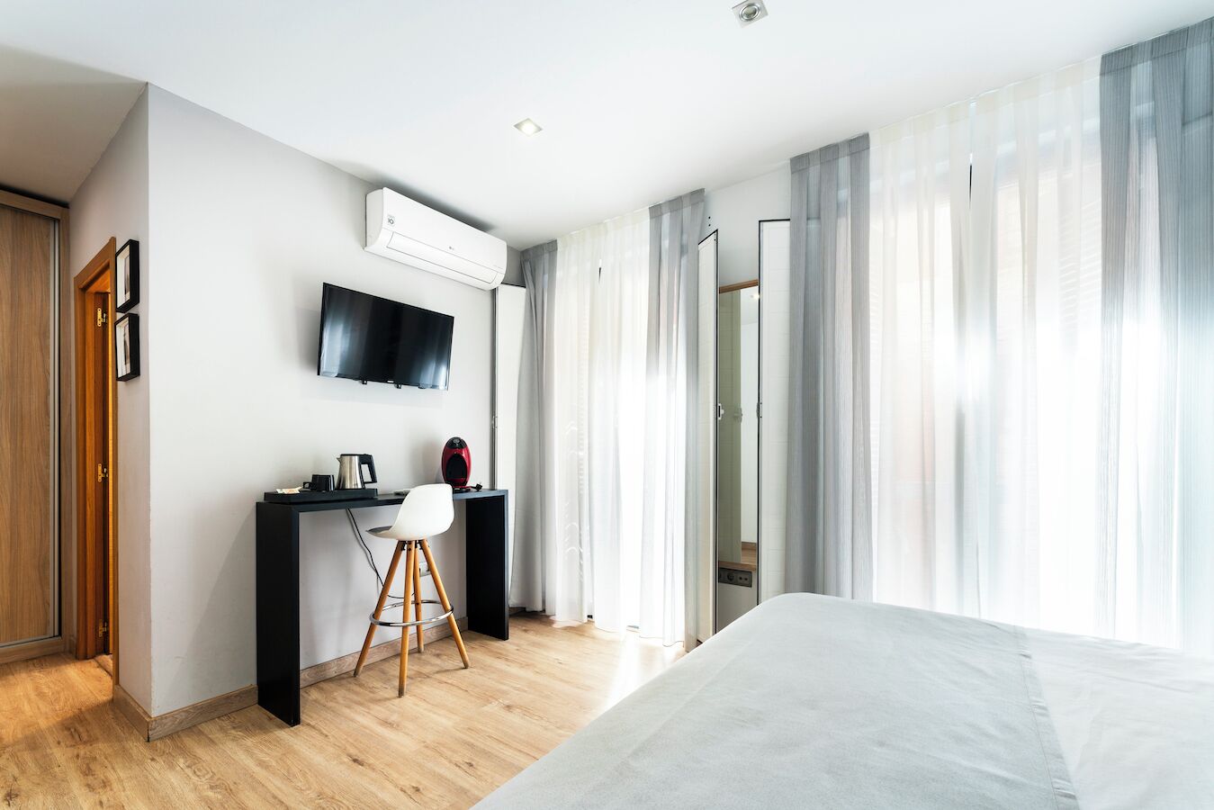 Een moderne hotelkamer met een bed, een bureau met stoel, een flatscreen-tv en een airconditioning.