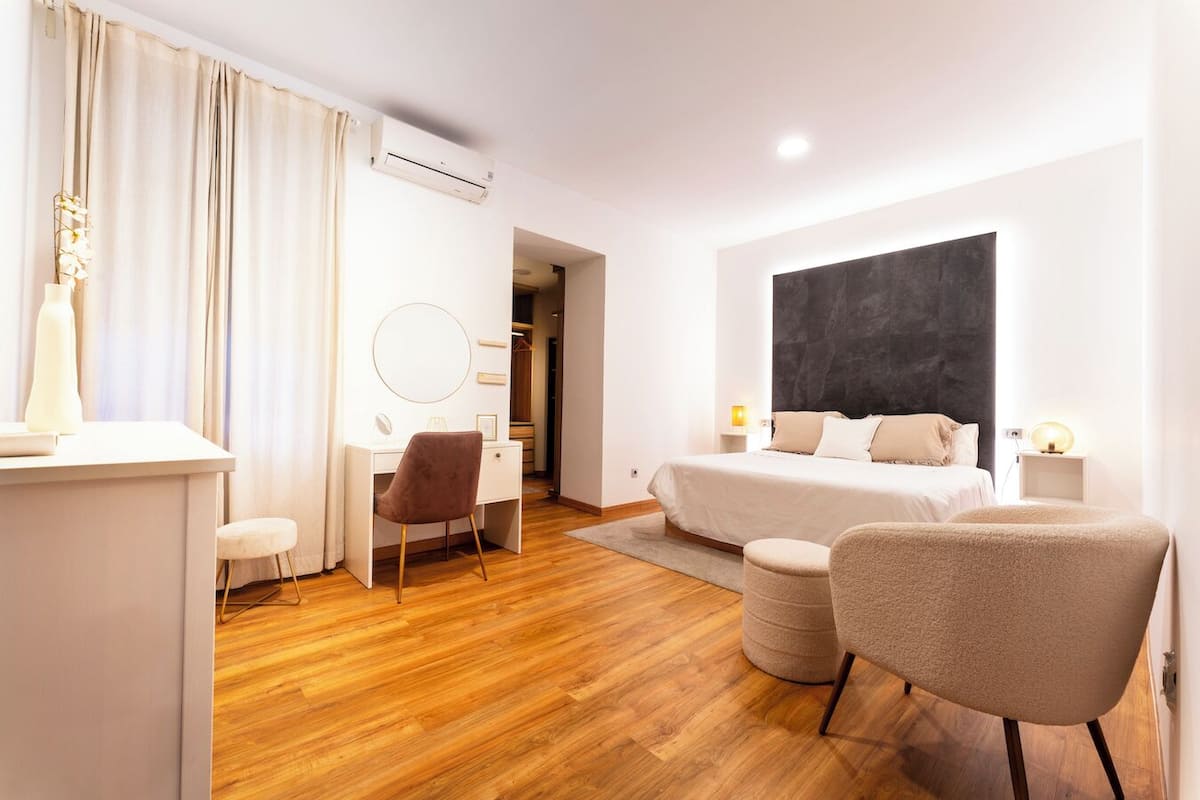 A modern bedroom with a bed, bedside tables, a desk, a chair, and a large abstract wall art piece.