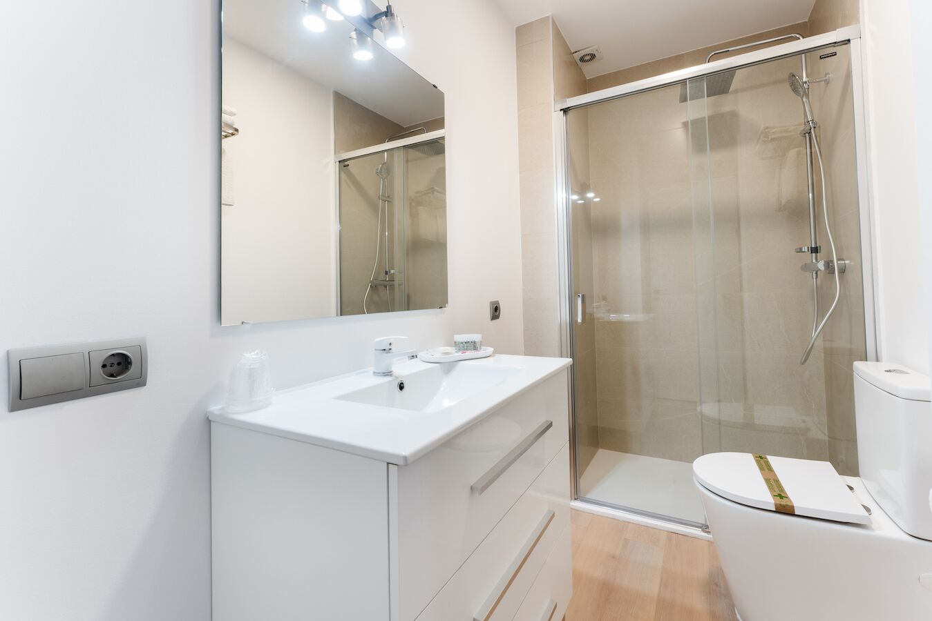 Un baño moderno con ducha de vidrio, lavamanos blanco y retrete.