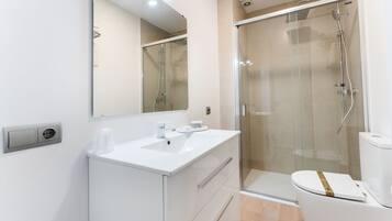 Un baño moderno con ducha de vidrio, lavamanos blanco y retrete.