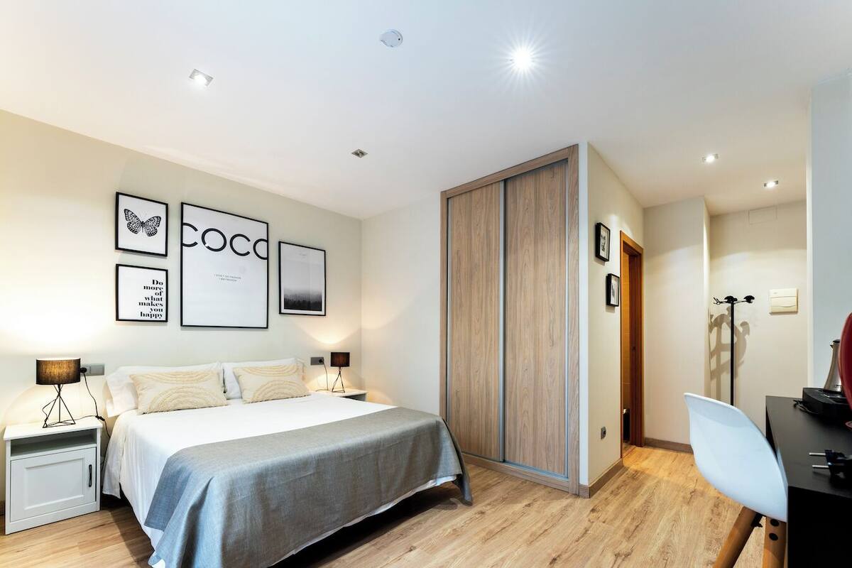 A modern bedroom with a bed, bedside tables, a wardrobe, and wall art.