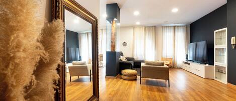 Una sala de estar moderna con un espejo grande, suelo de madera y un televisor sobre un mueble.