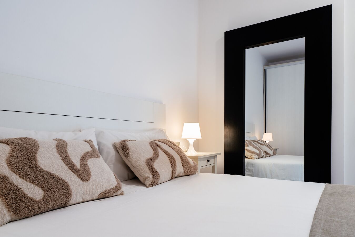 A hotel room with a bed, two bedside lamps, a nightstand, and a large mirror.
