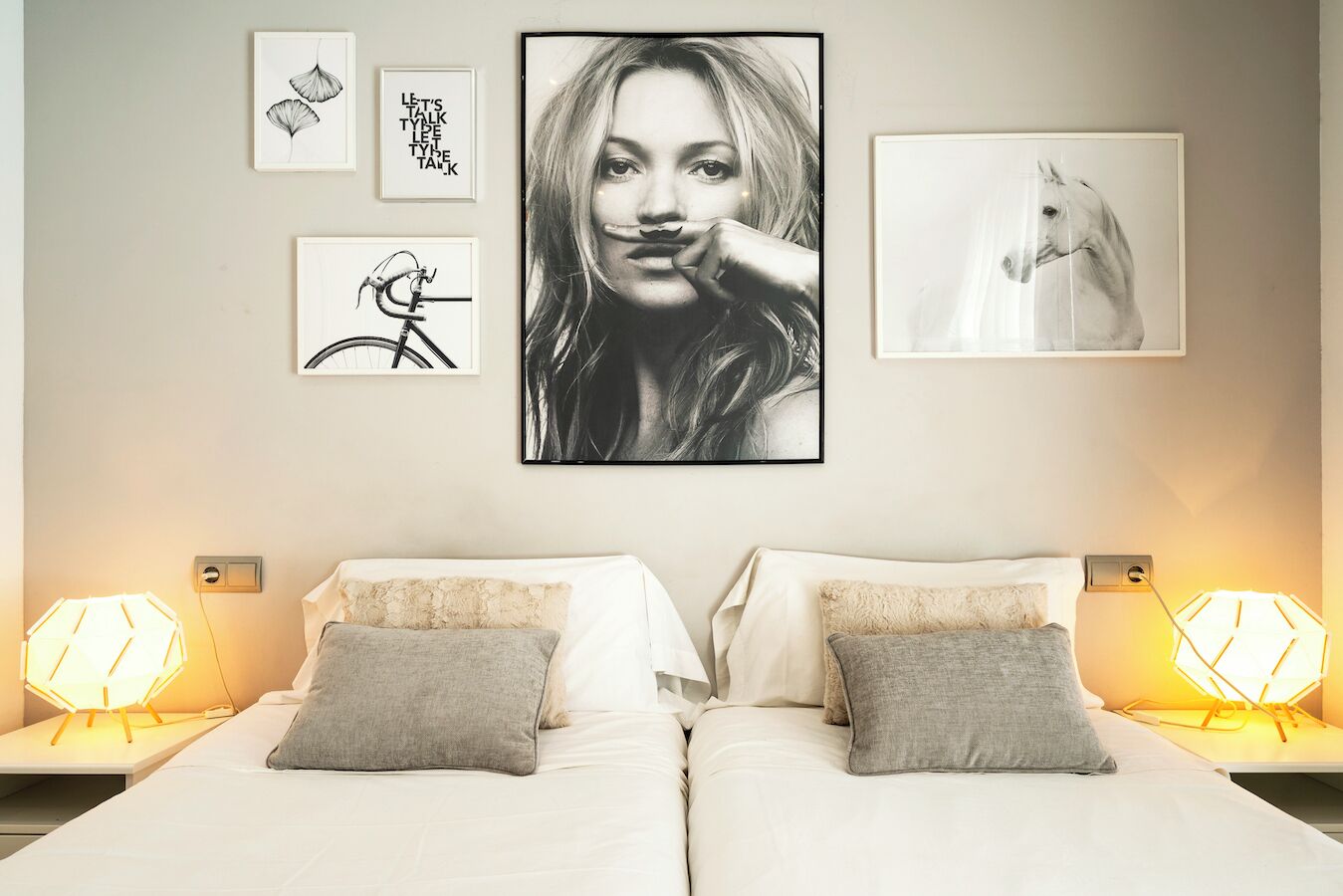 Un dormitorio con dos camas, una pared decorada con cuadros y lámparas de noche.