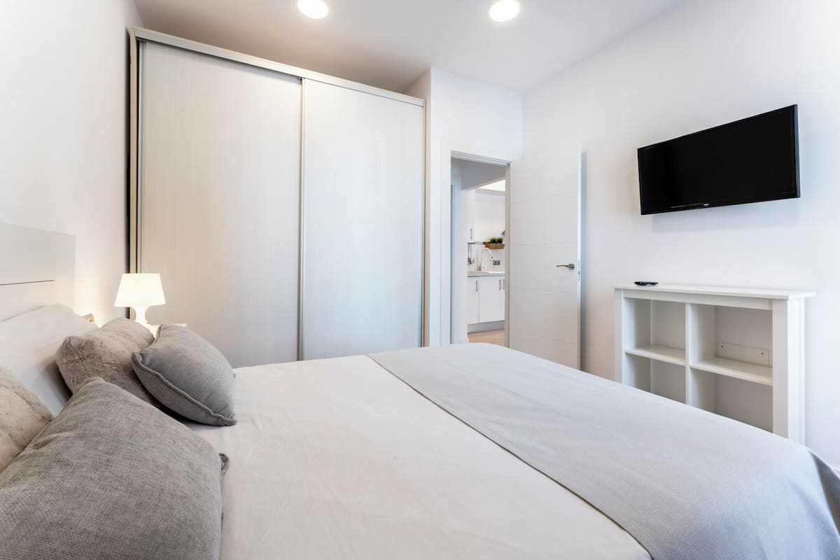 A bedroom with a bed, pillows, a nightstand, a TV, and a wardrobe.