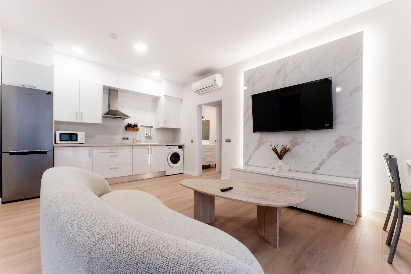 A modern kitchen with a built-in microwave, a washing machine, and a flat-screen TV mounted on a marble wall.