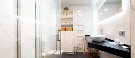 Ein modernes Badezimmer mit Duschkabine aus Glas, einer weißen Toilette, einem Waschbecken mit schwarzer Arbeitsplatte und einem Spiegel.