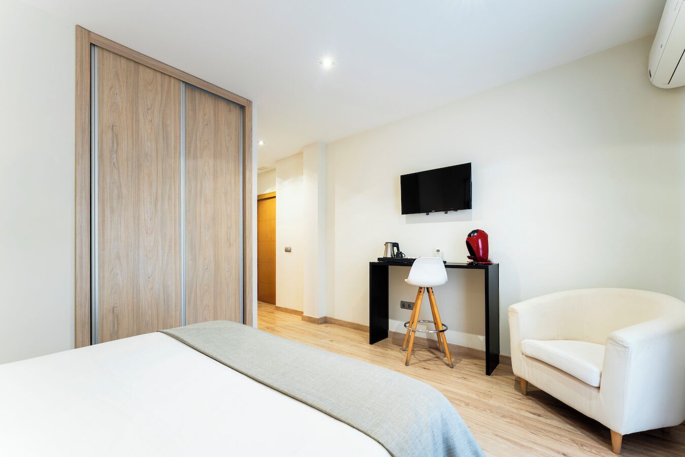 A hotel room with a bed, a desk, a chair, a TV, and a wardrobe.