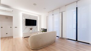 Een moderne woonkamer met een flatscreen televisie, een marmeren spatwand en een groot raam met jaloezieën.