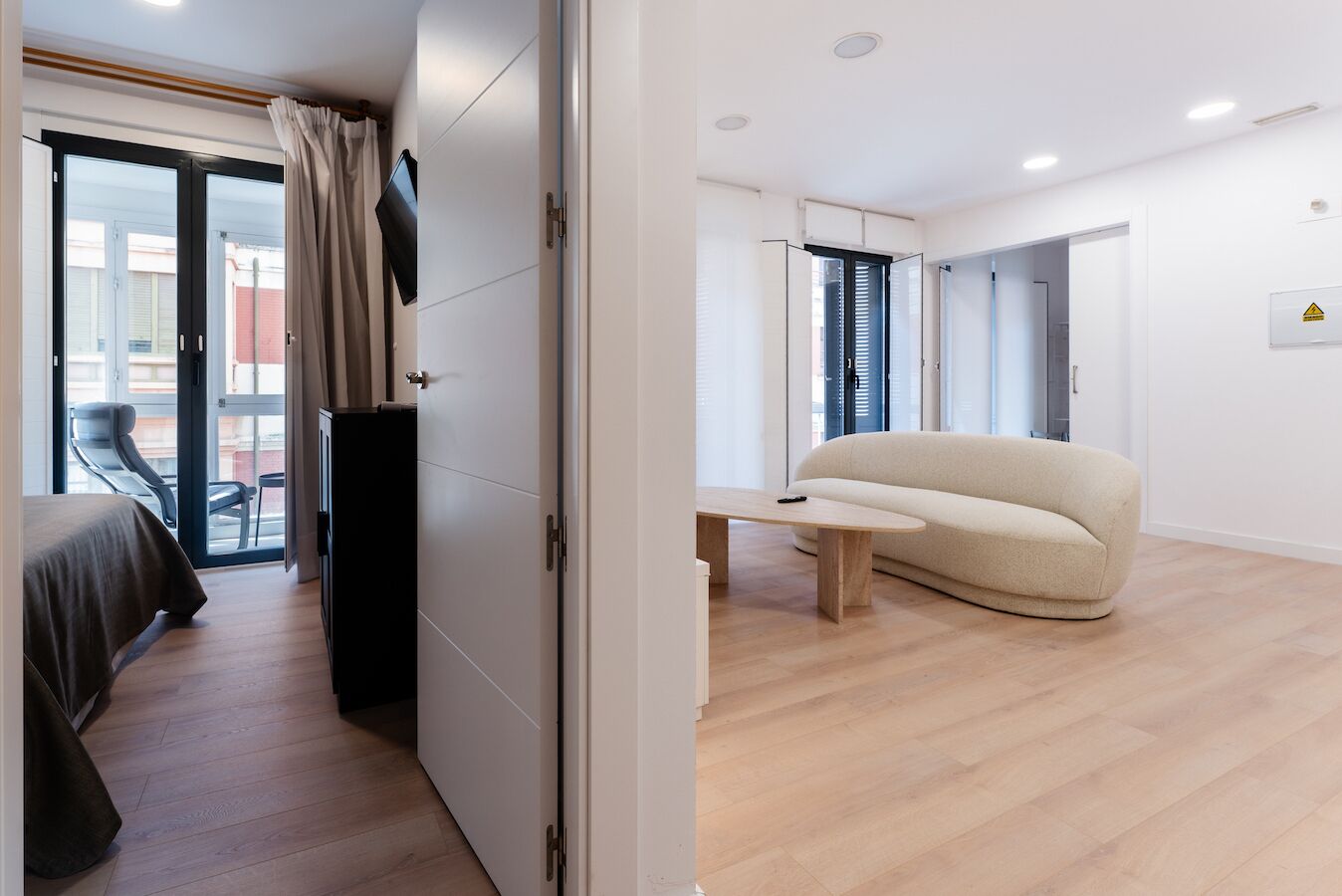 Une chambre d’hôtel moderne équipée d’un lit, d’un bureau, d’un canapé et d’une porte-fenêtre coulissante donnant sur un balcon.