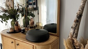 En byrå i trä med en spegel, en vas med torkade växter och en björkgren.