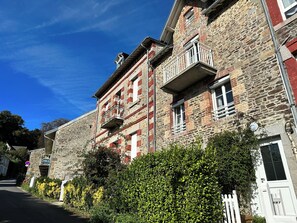 A stone building with multiple windows and balconies, surrounded by greenery and a clear sky. - Mont St Michel bay house (Saint-Jean-le-Thomas)