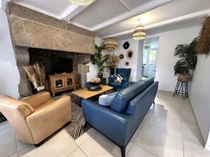 A living room with a stone fireplace, a blue sofa, a leather armchair, and a television. - Mont St Michel bay house (Saint-Jean-le-Thomas)