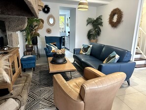 Un salon avec un canapé bleu, une table basse et un fauteuil en cuir. On y trouve également des éléments décoratifs accrochés au mur et une plante en pot.