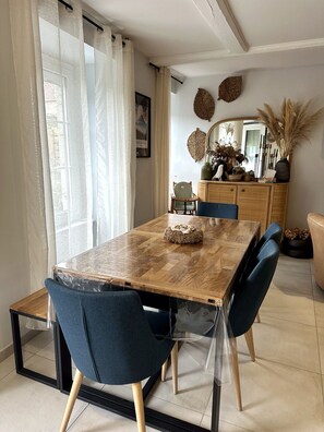 A dining area with a wooden table, blue upholstered chairs, and a glass-top table. - Mont St Michel bay house (Saint-Jean-le-Thomas)