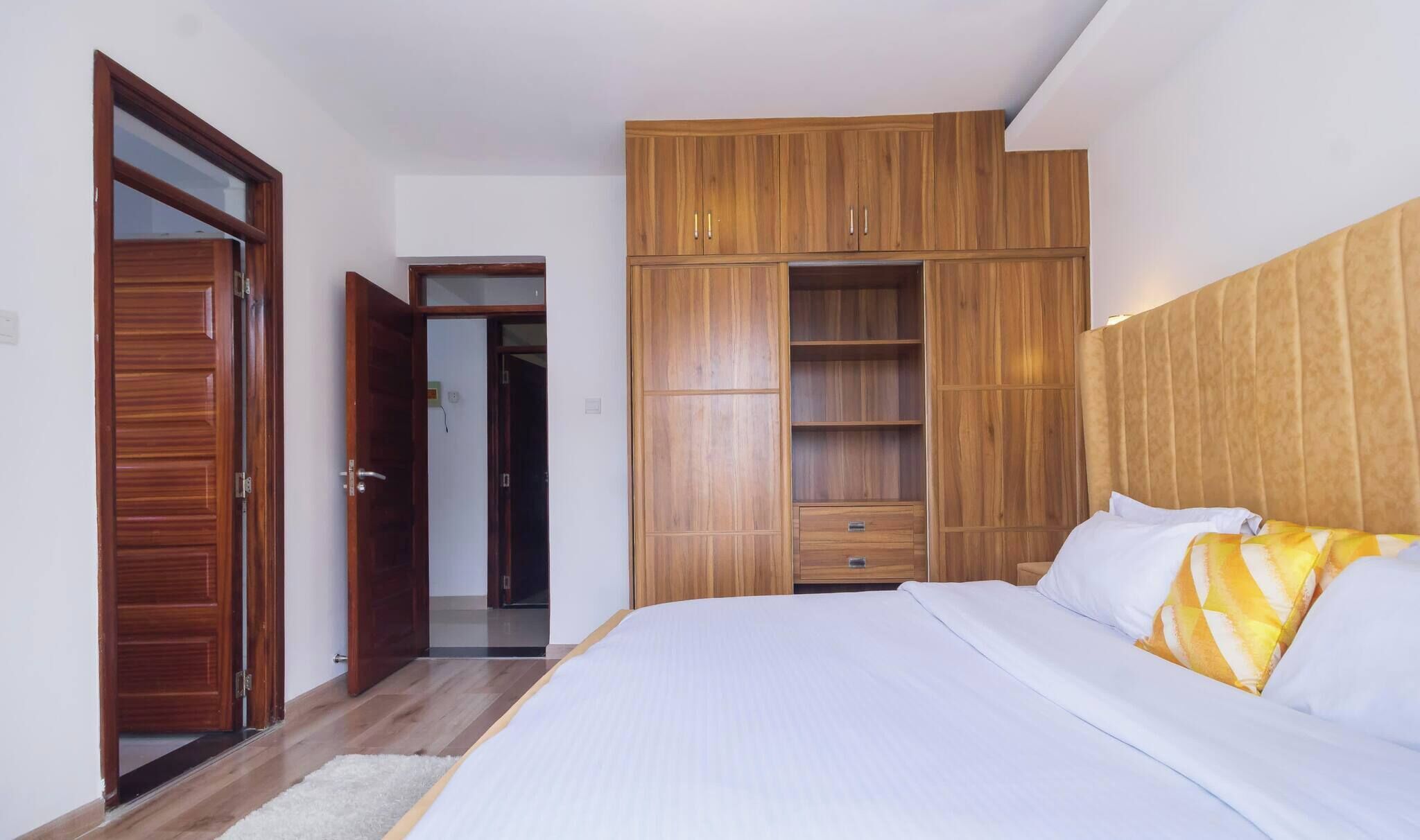 A bedroom with a bed, wooden wardrobe, and a door leading to another room.