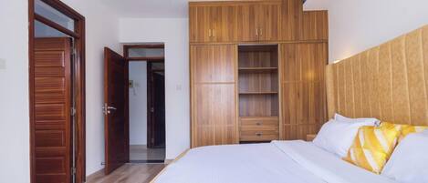 A bedroom with a bed, wooden wardrobe, and a door leading to another room.