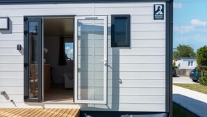 A compact mobile home with a door open, revealing an interior with a bed and a small table. - Caravan Bredene on the Coast (Bredene)