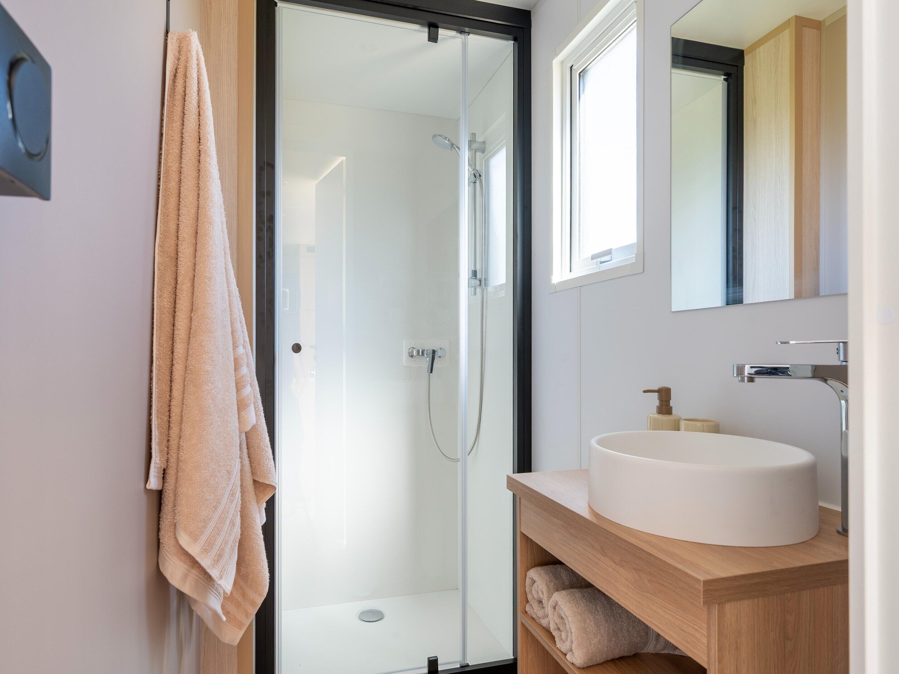 A modern bathroom with a glass shower door, a white sink, and a wooden vanity.