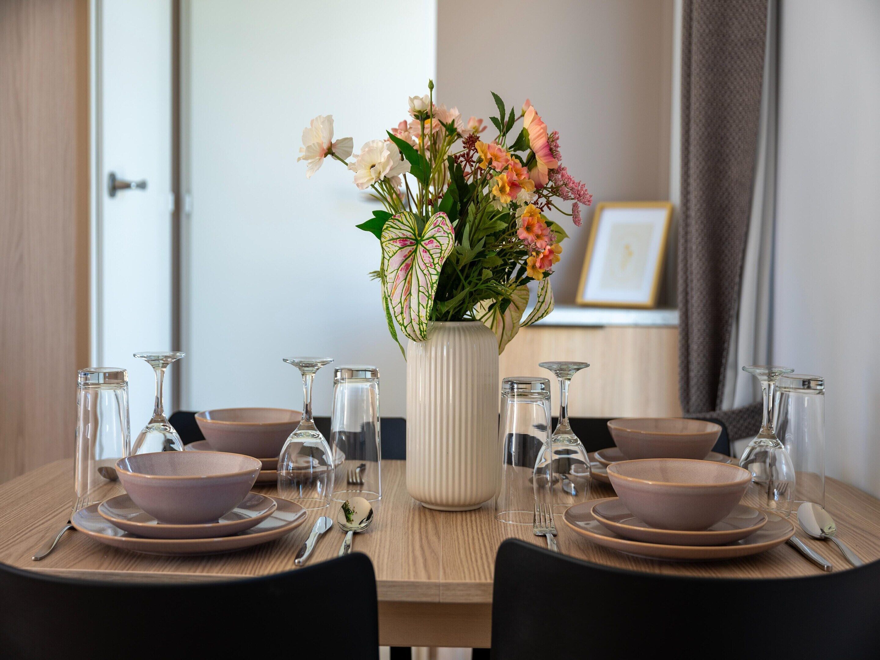 A dining table set with plates, bowls, cutlery, and a vase of flowers.