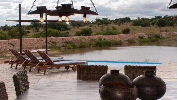 A poolside area with lounge chairs, a hanging light fixture, and rustic metal pots. - Casa de la Presa 3 (POLOKWANE)