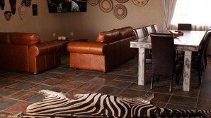 A living room with a brown leather sofa, a zebra rug, a TV, and a dining table with chairs. - Casa de la Presa 3 (POLOKWANE)
