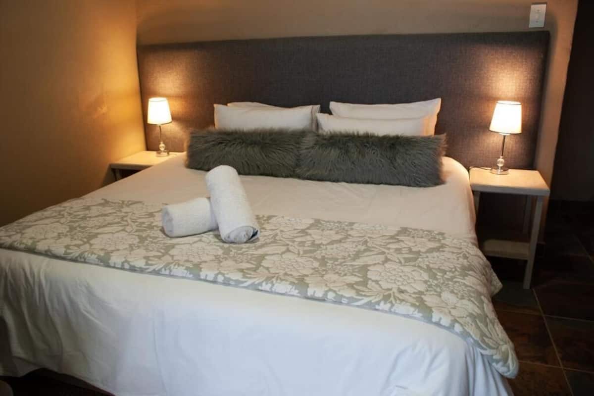 Una cama bien hecha con una colcha estampada con motivos florales, dos almohadas y una toalla enrollada. Hay dos mesitas de noche con lámparas, y la habitación tiene un diseño sencillo y limpio.