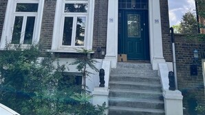 Een gebouw met twee verdiepingen, met een groene deur en witte details, huisnummer 96, met een veranda en treden die naar de ingang leiden.
