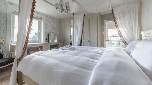 Een hemelbed met witte lakens, een kaptafel met spiegel en een kroonluchter.