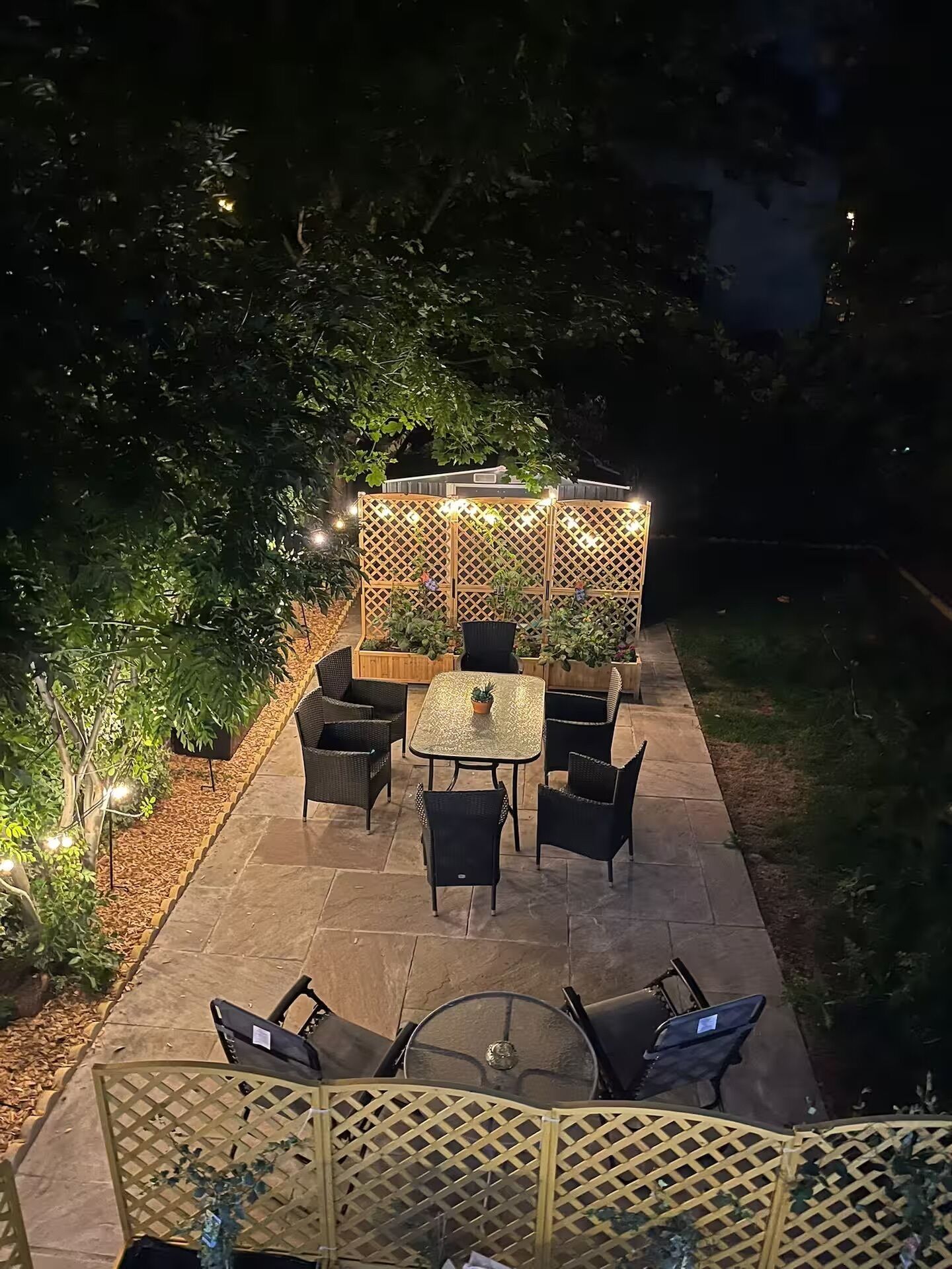 Un espace extérieur aménagé en patio, avec une table et des chaises, une clôture en bois et des guirlandes lumineuses.