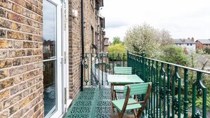 Een balkon met een bakstenen muur, een glazen deur en een groene balustrade.