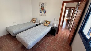 A room with two single beds, a small table with a lamp, a wall-mounted artwork, and a view through an open door. - Villa Erimar in cozy Playa Blanca (Playa Blanca)