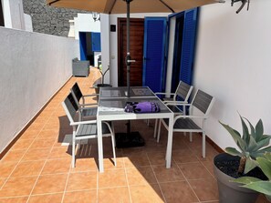 Eine Terrasse mit Tisch und Stühlen, einem Topfpflanzen und einer Tür mit blauen Fensterläden.