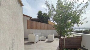 Un'area patio con mobili da esterno, un piccolo albero e una recinzione in legno.