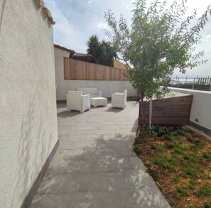 Eine Terrasse mit Gartenmöbeln, einem kleinen Baum und einem Holzzaun.