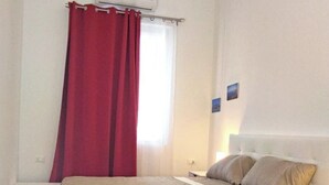 Una camera da letto con un letto, un comodino, un condizionatore d'aria a parete e una finestra con tenda rossa.